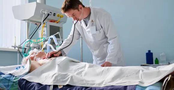 Un médecin vérifie le coeur d'un patient couché dans un lit et relité à une machine respiratoire