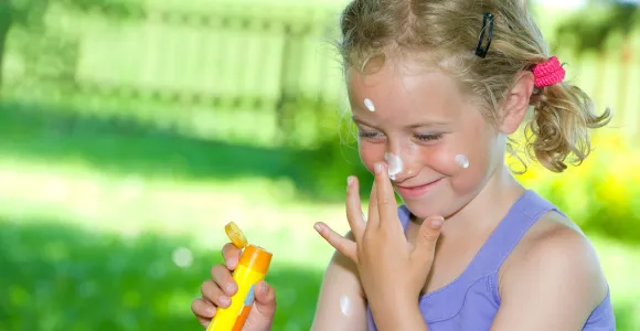 une petite fille s'applique de la crème solaire sur le visage