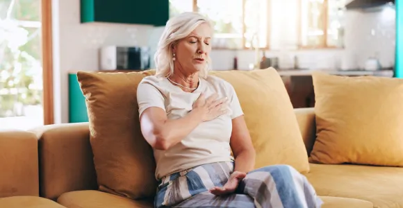 Une femme est assise sur un fauteuil, ferme les yeux et met sa main sur son coeur