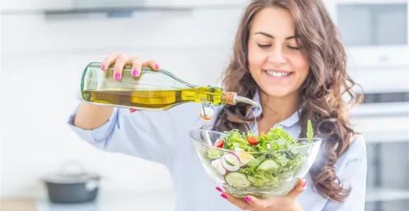une jeune femme fait couler de l'huile d'olive dans la salade