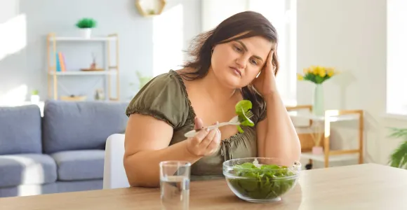 Une jeune femme mange avec désintérêt une salade 