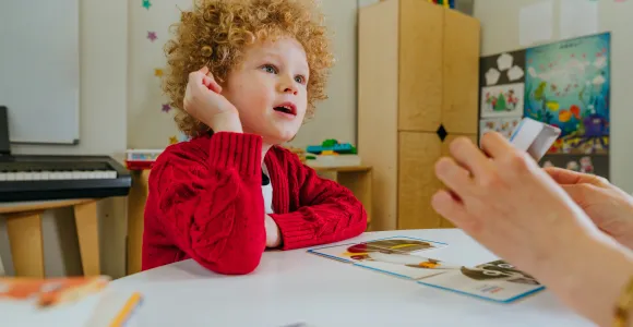 Enfant assis à une table, observant ce qu'un adulte lui montre.