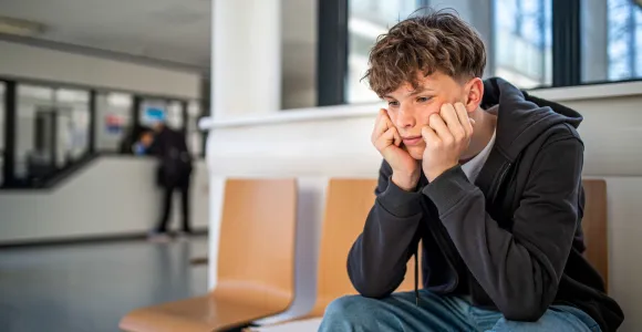 un jeune à la mine sombre se prend le visage dans les mains