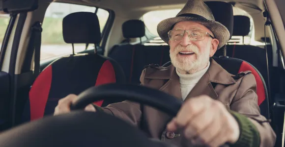 Un homme âgé tout sourire au volant de sa voiture