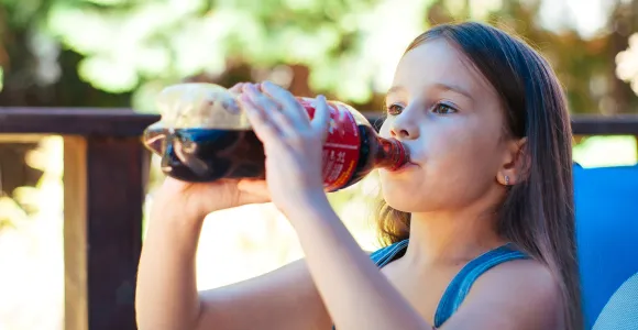 une enfant boit à la bouteille de coca