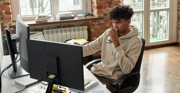 Un jeune homme boit une canette d'Energy Drink devant son ordinateur