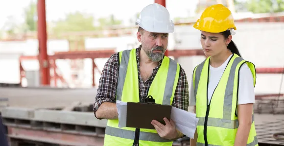 Une femme et son collègue regardent ensemble un document sur chantier