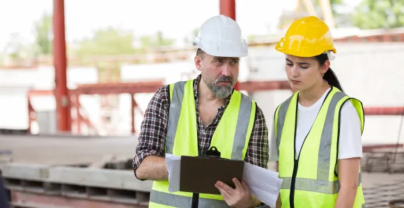 Une femme et son collègue regardent ensemble un document sur chantier