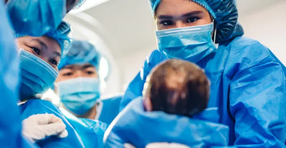 une sage femme tient un enfant dans ses mains lors d'un accouchement très médicalisé