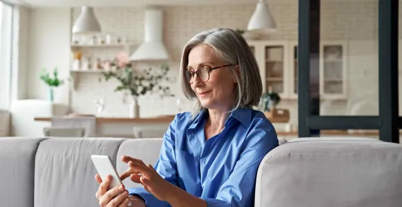 Une dame assise dans son fauteuil regarde son écran de téléphone