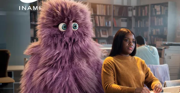 Une jeune femme assise dans un bibliothèque avec à l'arrière d'elle une grosse peluche