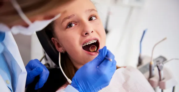 Une enfant est chez l'orthodontiste et montre ses dents et son appareil.
