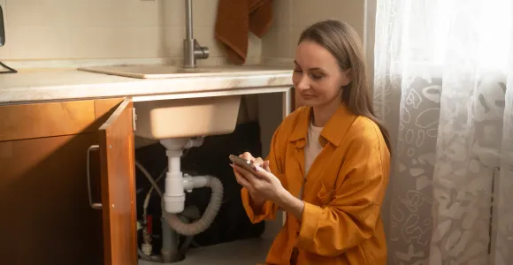 Une jeune femme examen la plomberie en dessous de l'évier de cuisine