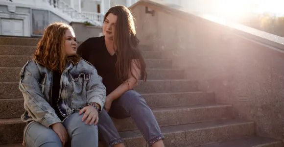 Deux jeunes filles discutent assises sur un escalier au soleil