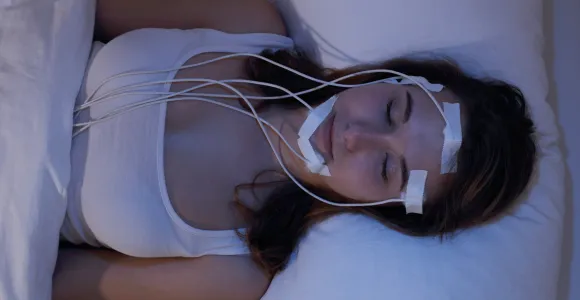 Une jeune femme étendue sur un lit, sous électrodes