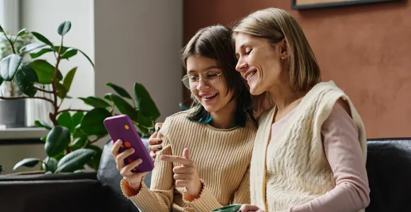 Une adolescente et sa maman regardent un écran de smartphone assise sur un fauteuil