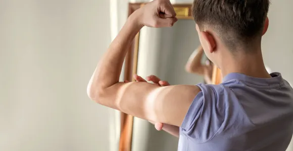Un ado mesure sa musculature devant le miroir