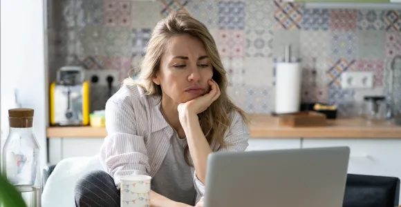 Une femme de la quarantaine regarde son ordinateur l'air dépité