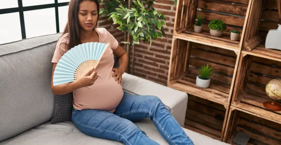une femme enceinte assise dans un canapé souffrant de la chaleur