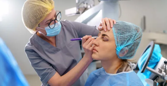 un chirurgien dessine des traits sur le visage d'une patiente avant l'opération.