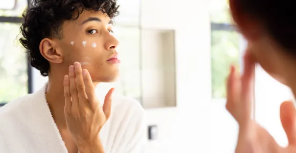 Un adolescent met de la crème sur sa peau