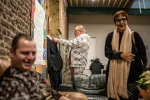 Deux bénéficiaires en train de rire avec d'autres personnes. derrière eux, un jeune homme ajuste le costume d'un mannequin à l'entrée de la donnerie du lieu. 