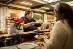 Héléna, bénéficiaire de la Croisée sert la salade liégeoise à une autre personne. 