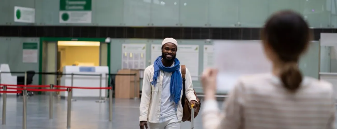 Homme voyageur arrivant avec une valise jaune vers une femme dans un hall d'aéroport.