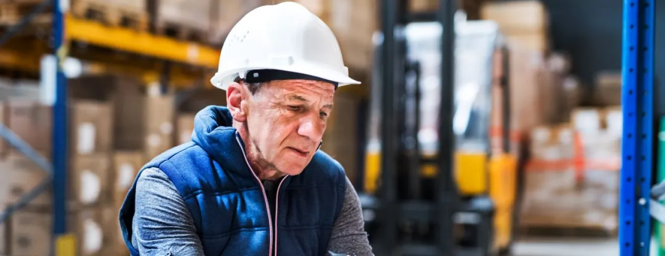 homme avec un casque de chantier sur la tête qui encode des données dans un appareil à l'intérieur d'un hangar