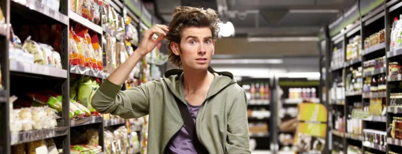 Jeune homme confus dans un rayon de pâtes d'un supermarché. 