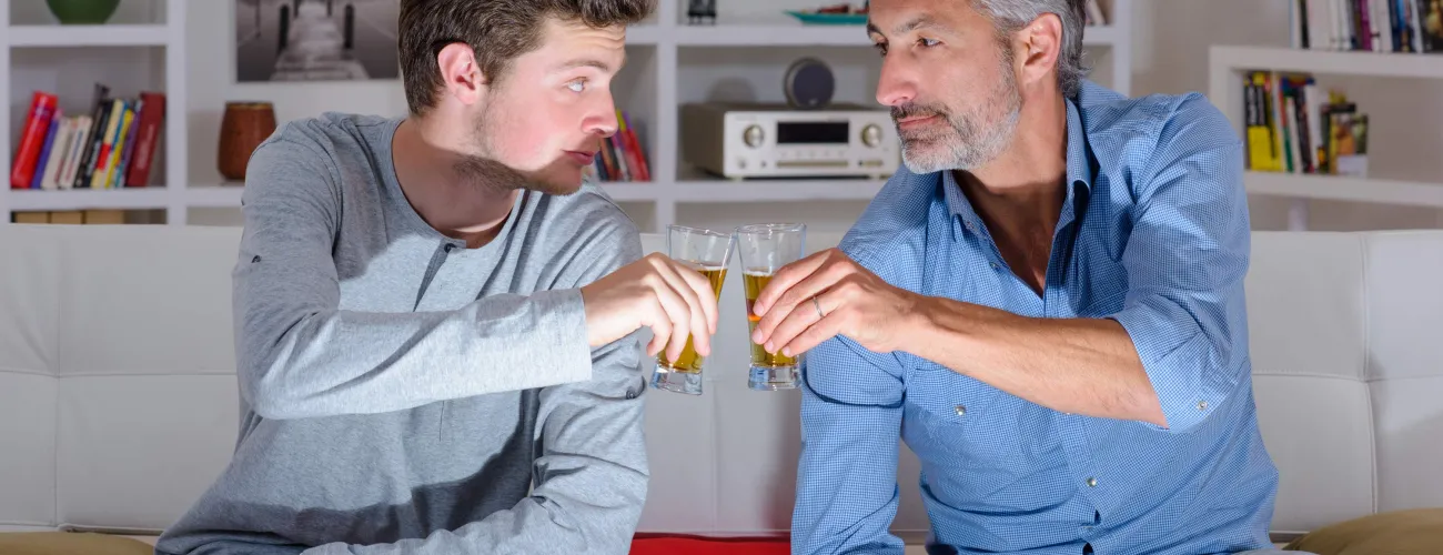 Un père et son fils  trinquent avec des shots d'alcool