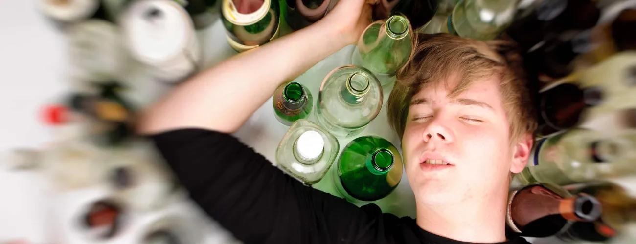 Un jeune couché entouré de bouteilles d'alcool vides
