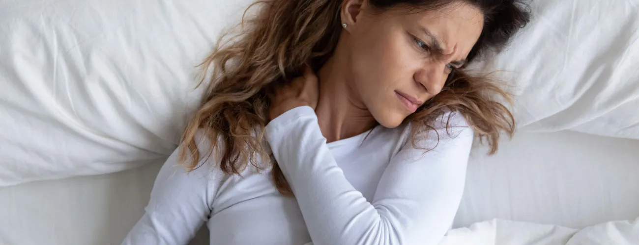 Une femme se tient le cou de douleur allongée dans son lit
