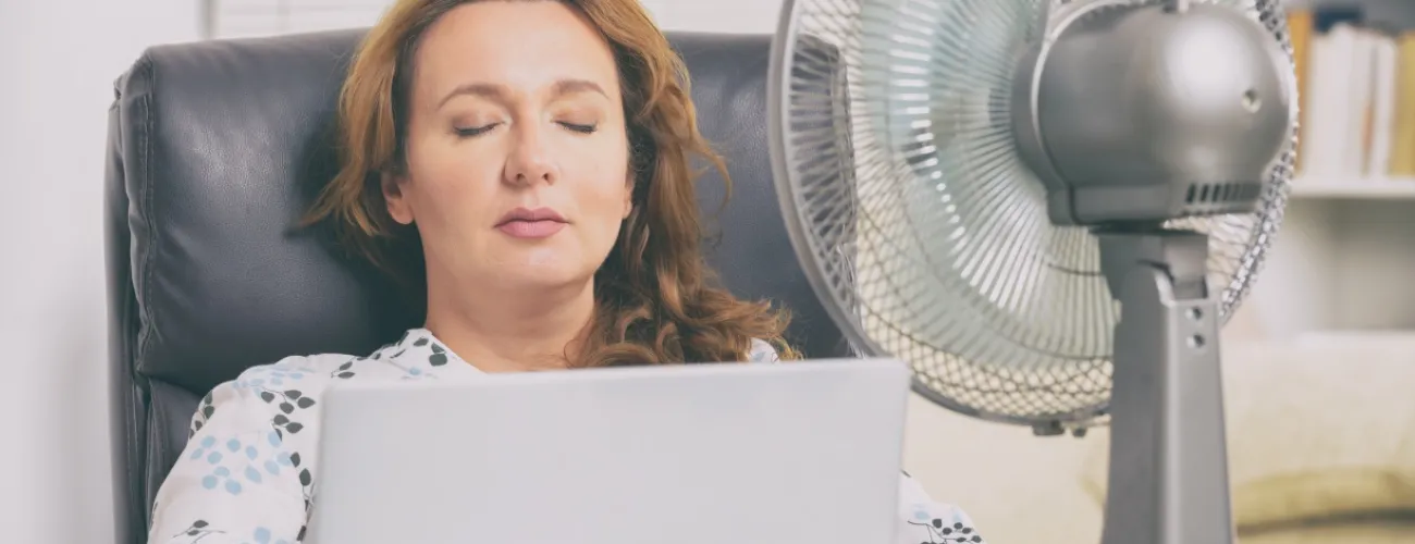 Femme assise sur un fauteuil un ventilateur lui souffle de l'air sur le visage