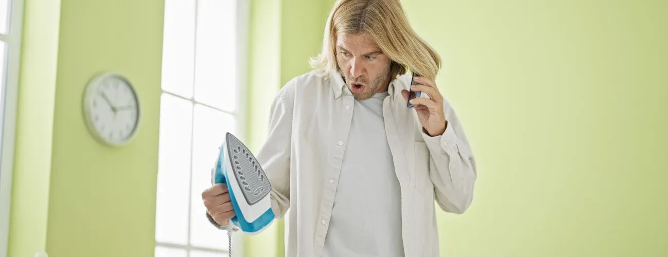 Homme paniqué avec un fer à repasser dans une main et un téléphone à l'oreille