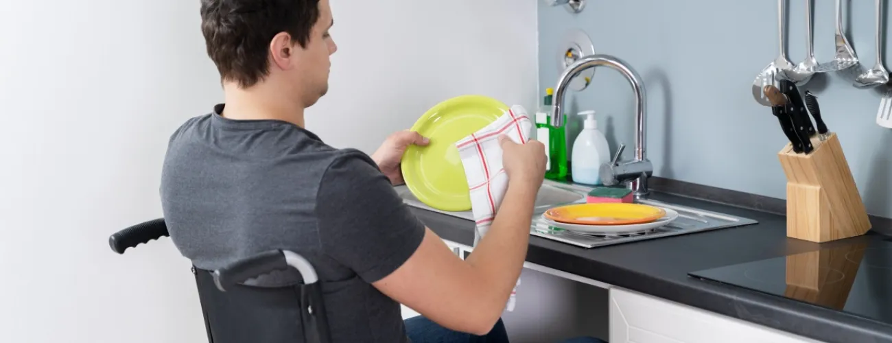 Une personne en chaise roulante fait la vaisselle à son domicile