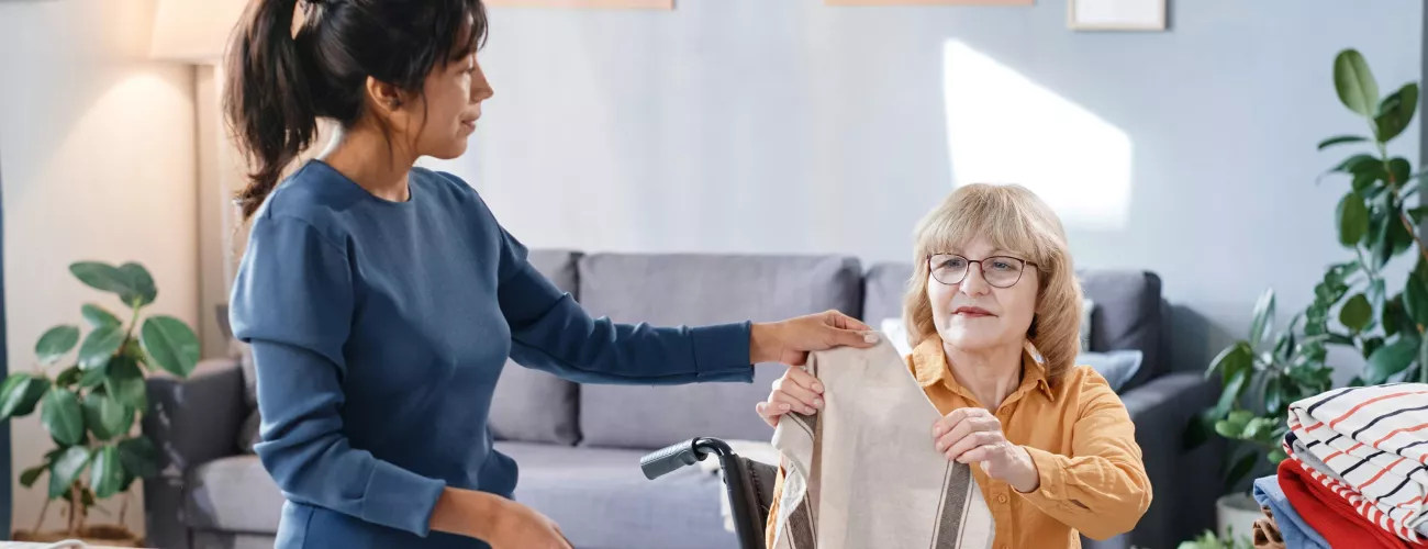 Une aide ménagère sociale aide une dame en chaise roulante pour le repassage