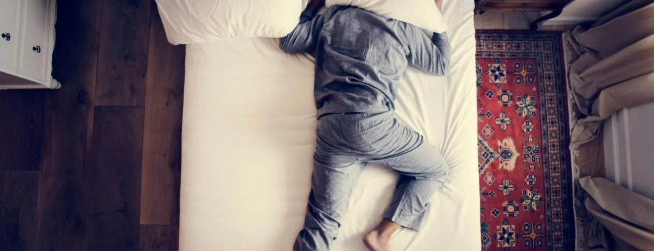 homme endormi sur un lit la tête sous un coussin 