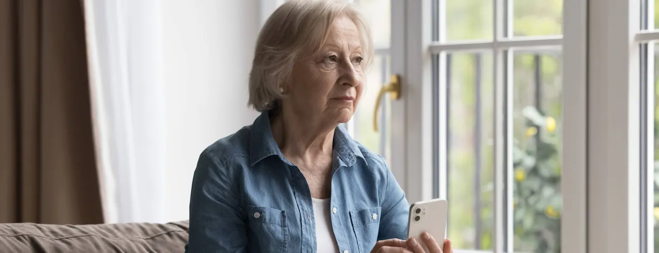 Une dame âgée assise sur un fauteuil tient un smartphone en main