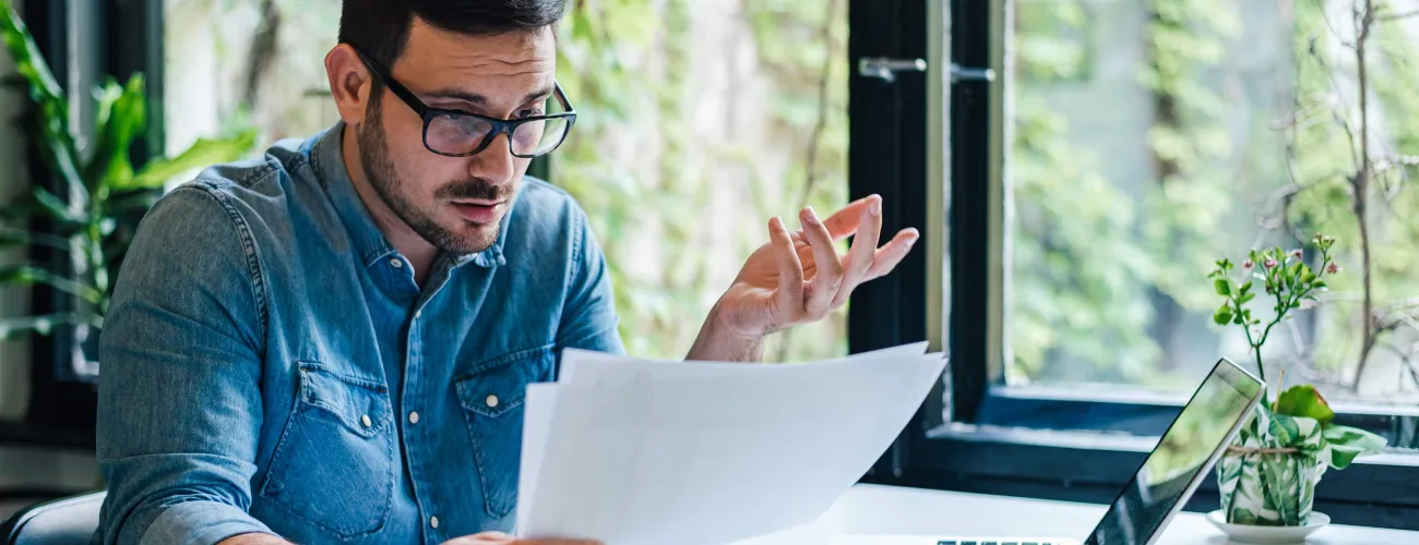 Un homme dubitatif en train de remplir sa déclaration fiscale devant son ordinateur