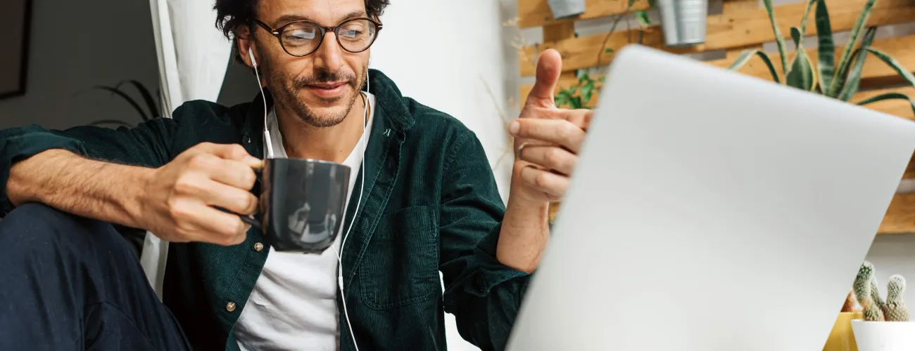 Un homme en télétravail boit un café derrière son ordinateur