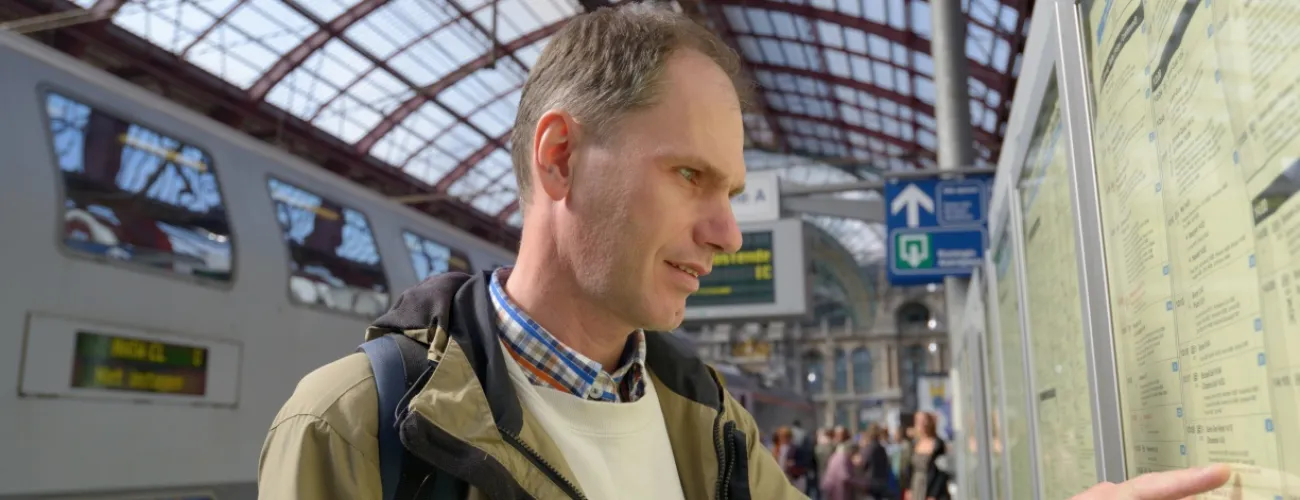 Un homme sur le quaie d'une gare regarde les horaires des trains