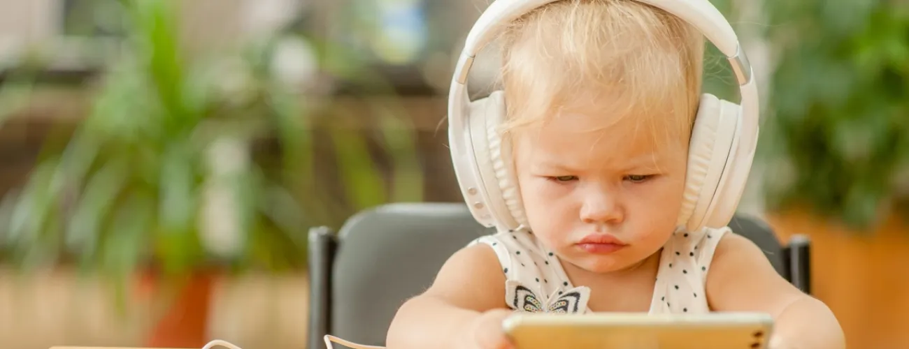 Un enfant en bas age porte un casque audio et regarde un écran de téléphone