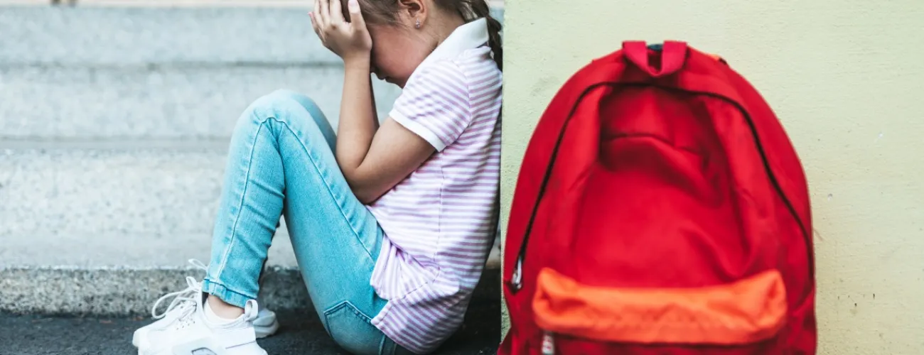 Fillette assise dos au mur le visage dans les mains