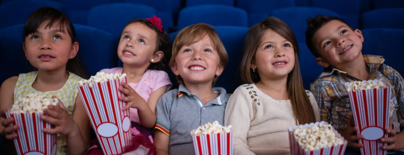 Cinq enfants assis dans une salle de cinéma avec des popcorns dans les mains