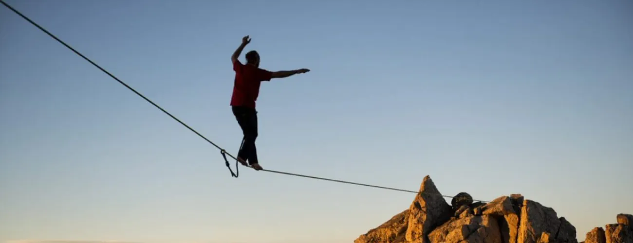Un équilibriste marche sur un fil tendu vers une montagne