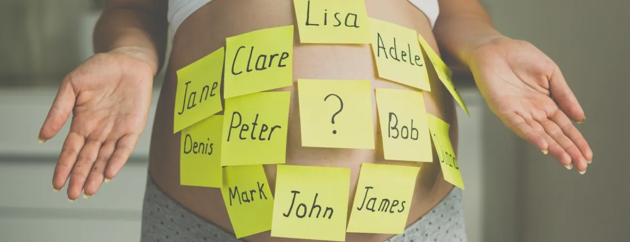 Photo d'un ventre de femme enceinte avec des post-it collés dessus sur lesquels sont écrits des prénoms