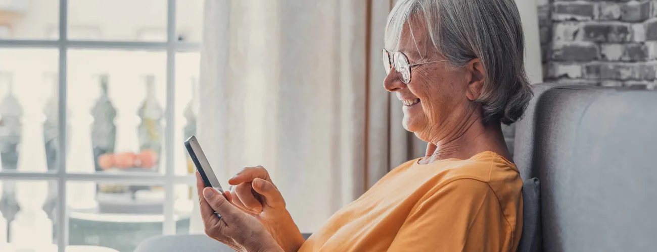 Une dame âgée assise dans un fauteuil consulte son smartphone