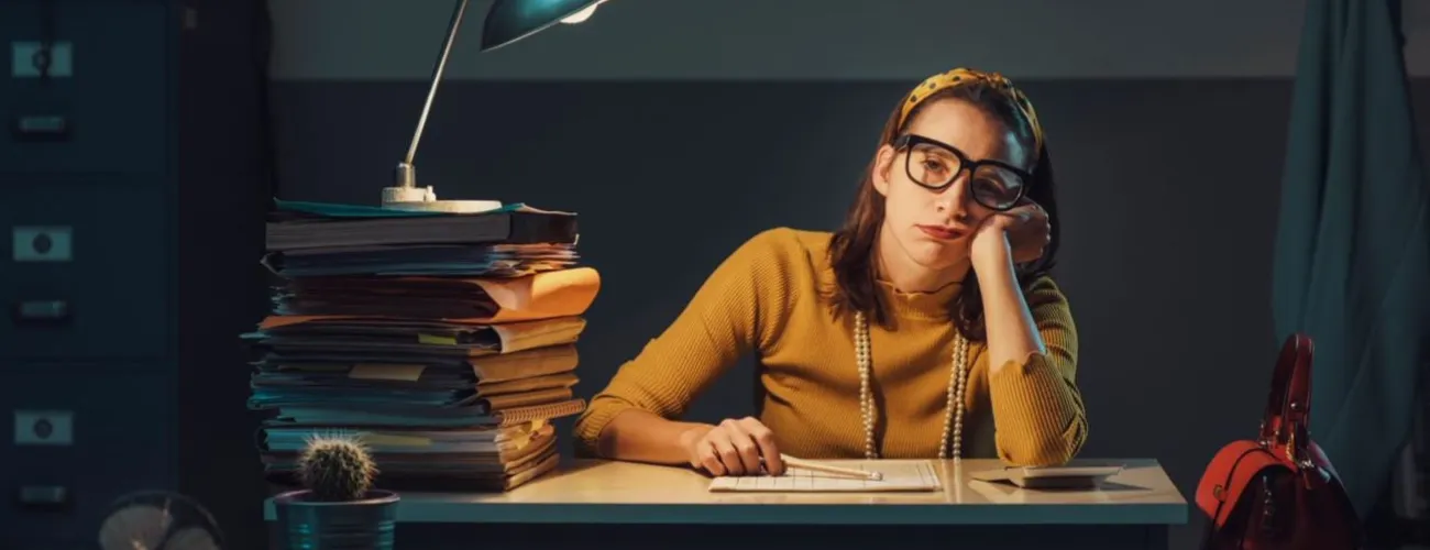 Femme dépitée assise sur un bureau entourée de piles de documents