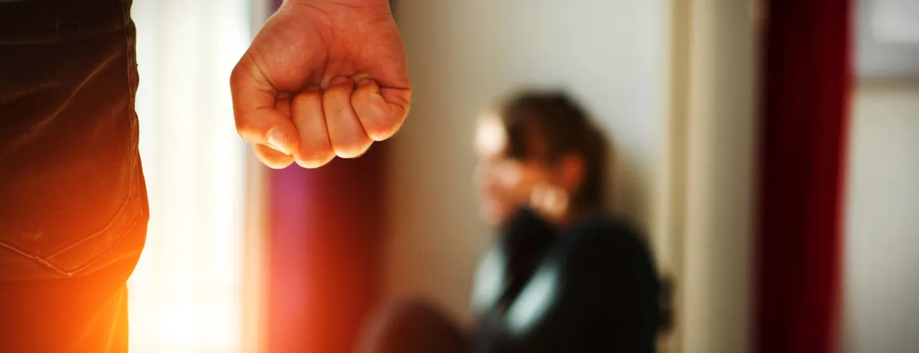 Un homme le poing serré se dirige vers une femme se protégeant au sol